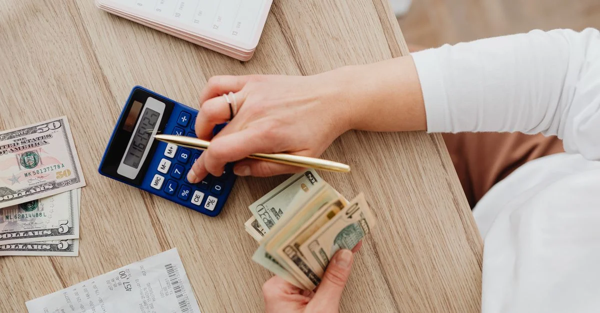 Personne utilisant une calculatrice et comptant de l'argent sur une table en bois avec des reçus.