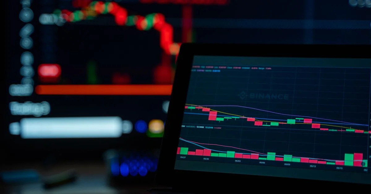 Un bureau faiblement éclairé affichant des graphiques de trading de cryptomonnaies sur plusieurs écrans.
