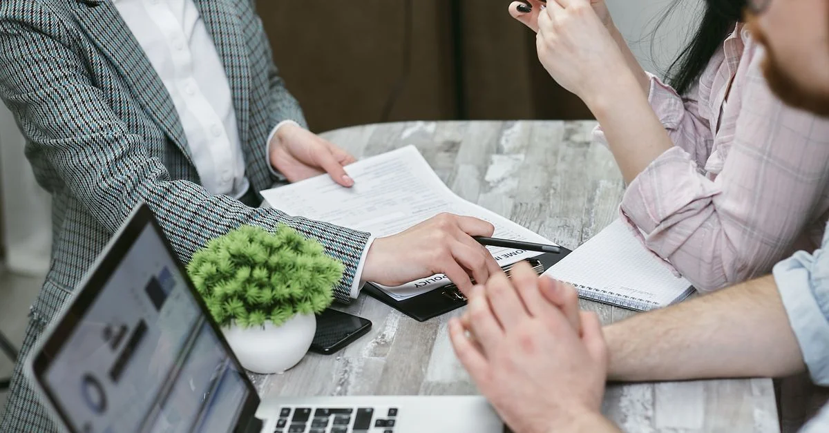 Réunion professionnelle discutant d'accords commerciaux avec des ordinateurs portables et des documents sur une table rustique.